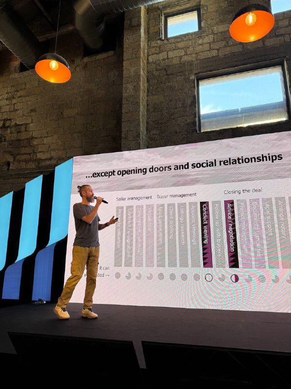 Single presenter on stage at Elevate Summit speaking in front of a large slide about opening doors and social relationships in an industrial-style venue.