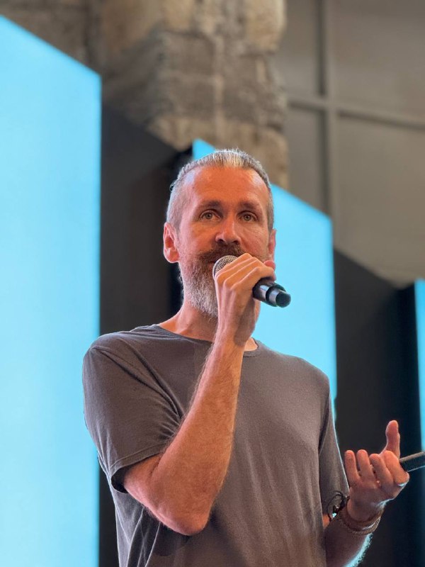 Close-up of a speaker holding a microphone on stage at Elevate Summit during a PropTech talk, photographed against a blue stage backdrop.