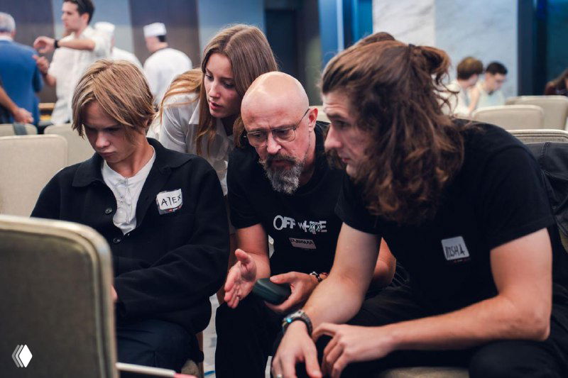 Small group of hackathon participants collaborating with a mentor: discussion over phones and notes, intensive teamwork and problem solving visible.