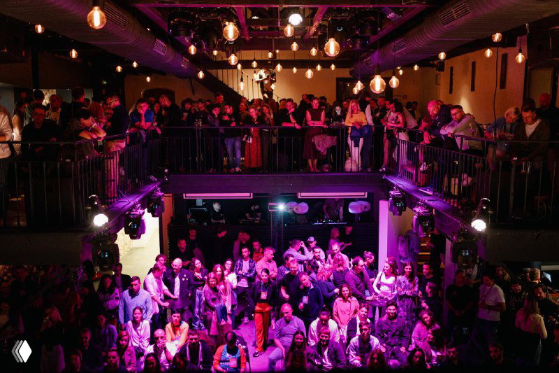 Crowd shot showing attendees mingling and watching the stage under decorative lighting inside the Lisbon venue during the Future Unicorns Party.