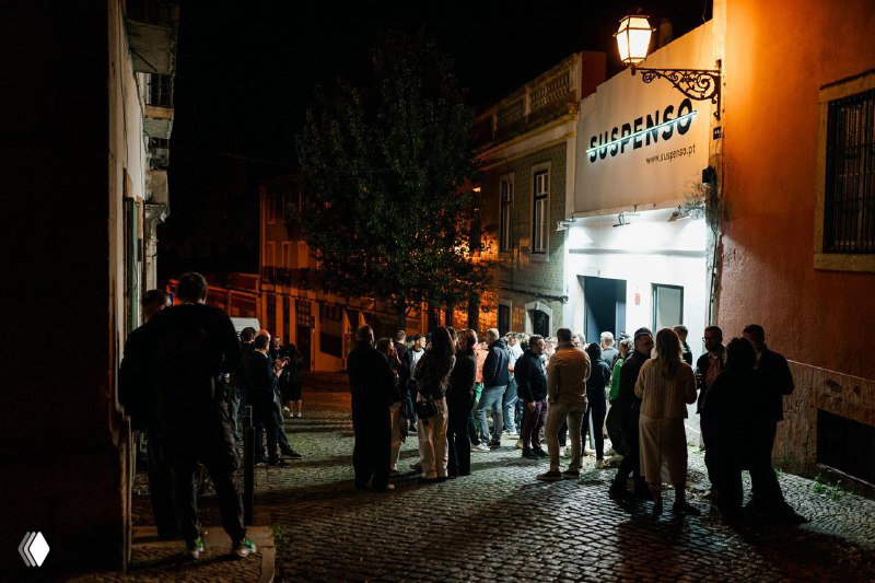 Exterior night photo of a queue of people outside the venue in Lisbon for the Future Unicorns Party 2025, cobblestone street and venue sign visible.