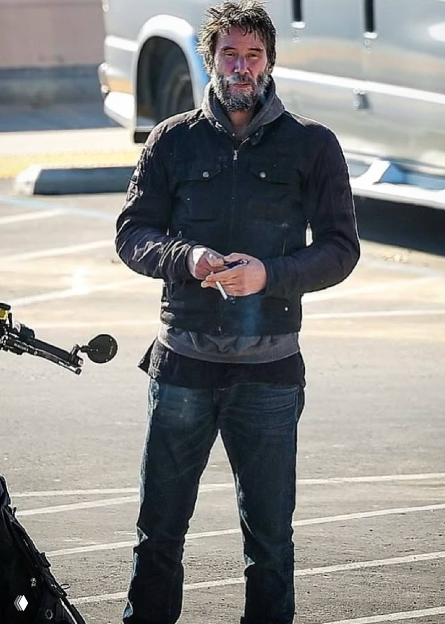 Мужчина на парковке в демисезонной одежде, держит в руках предмет, вокруг видна городская среда и рабочая техника, спокойный повседневный портрет.