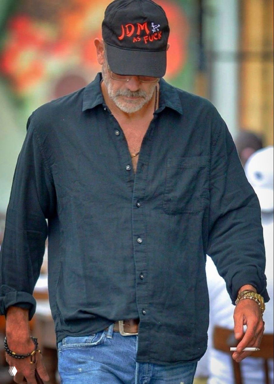 Мужчина в тёмной рубашке и кепке идёт по улице, опущенный взгляд; снимок передаёт повседневную сдержанность и приватность образа.