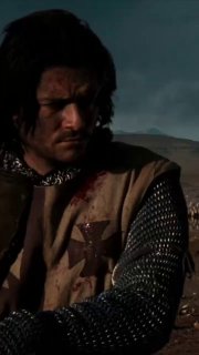 Крупный план рыцаря в средневековом одеянии и кольчужной рубахе с крестом на нагруднике — напряжённый кадр из фильма «Царствие небесное», героическая сцена в пустынном пейзаже.