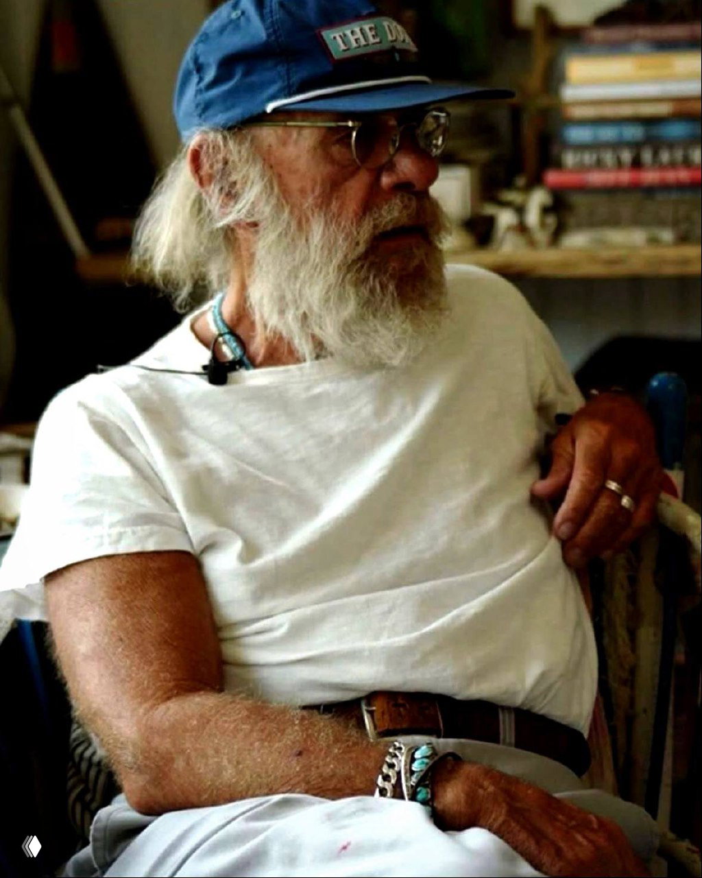 Старик с бородой и кепкой сидит в мастерской; кадр передаёт ощущение ремесленника, прожитой жизни и рассказа через детали интерьера.
