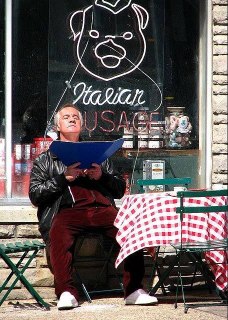 Персонаж сидит на уличной скамье перед витриной с неоновой надписью Italian Sausage — городской антураж и повседневная сцена из жизни героев.