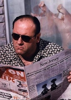 Тони в солнцезащитных очках читает газету New Jersey на скамье — кадр подчёркивает местный колорит и рассудительный образ персонажа перед действиями.