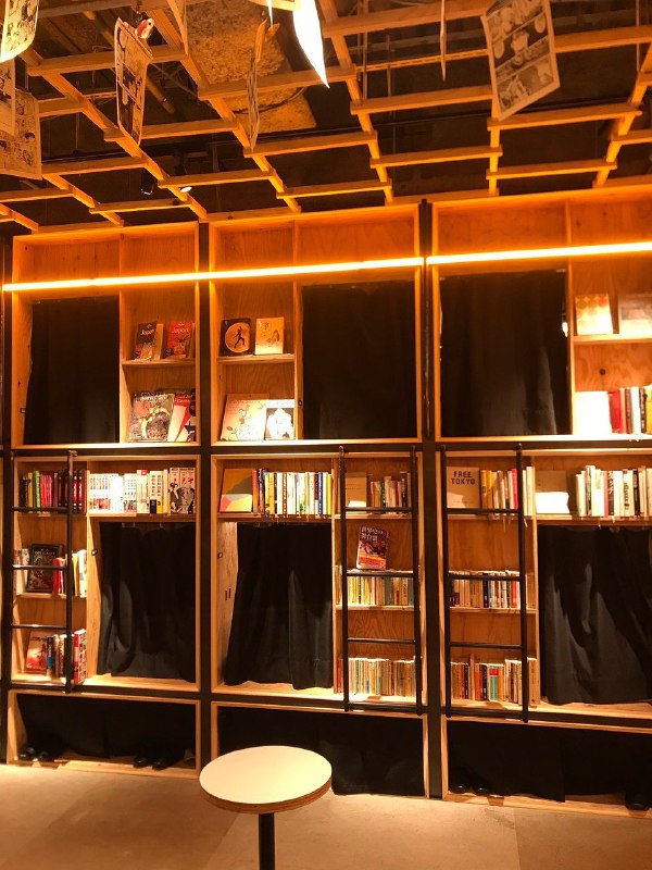 Стеллажи с книгами и небольшие столики у оконных ниш, вид на рабочие и отдыхательные зоны в Book and Bed, Токио.