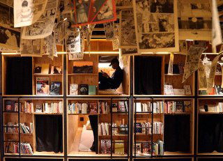 Капсулы с небольшими окнами и читателем внутри, уютный уголок для сна и чтения в Book and Bed, декоративные книги вокруг.