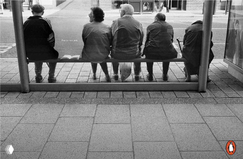 Чёрно-белый уличный кадр: скамейка с раскрытой книгой рядом с несколькими сидящими людьми; городской тротуар и витрина на заднем плане.