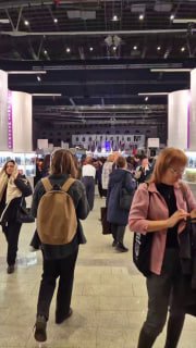 Посетители идут по центральному проходу выставки non/fiction: люди в верхней одежде, фон из витрин и стендов, оживлённая атмосфера мероприятия.