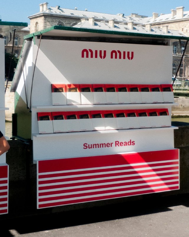Несколько стендов с логотипом Miu Miu и надписью Summer Reads — стильная торговая установка бренда с красно‑белой отделкой и полками для книг.