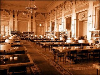 Сепия-фотография читального зала Исторической библиотеки: пустые столы с настольными лампами, резной декор и тёплый рассеянный свет.