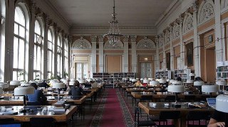 Широкий план читального зала Исторической библиотеки с рядами столов, редкими читателями и большой центральной люстрой — интерьер и столы.