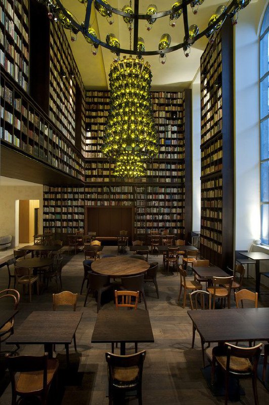 Общий вид читального пространства библиотеки отеля B2: ряды столов, деревянная мебель и высокая книжная стена как фон.