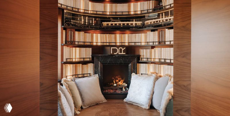 Уютная ниша с камином в библиотеке вагона: каминный портал, округлая лавка с подушками и тёплая атмосфера для чтения и отдыха.