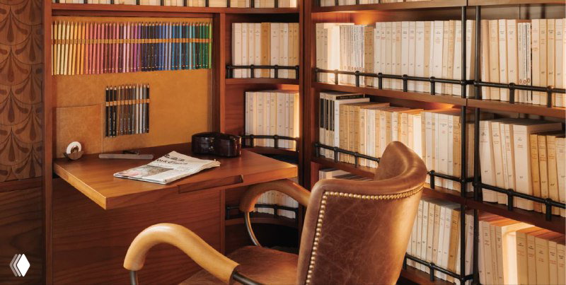 Рабочий кабинет с библиотекой в сьюте: письменный стол из дерева, кожаное кресло и полки с собранными томами вокруг рабочего места.