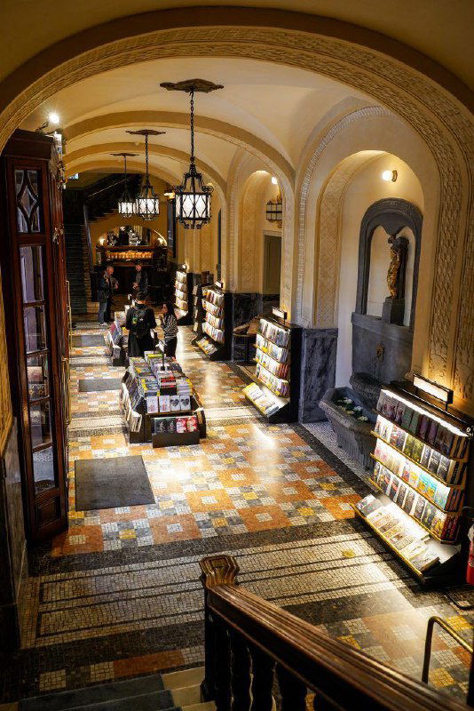 Коридор и лестница внутри Giunti Odeon: книжные полки вдоль стены, мраморный пол и атмосферное теплое освещение в стиле старинного интерьера.