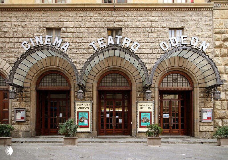 Фасад Giunti Odeon во Флоренции: три арочных входа с вывесками «Cinema Teatro Odeon», каменная облицовка и вывески у дверей.
