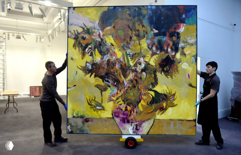 Два человека переносят огромный холст с ярким цветочным мотивом; видно ощущение масштаба и театральность работы.