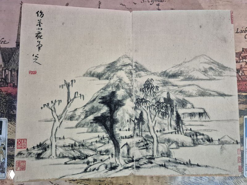 Один разворот с тушевым пейзажем: горы, деревья и постройки в традиционной манере шань‑шуй, на бумаге видны печати и каллиграфия в углу.