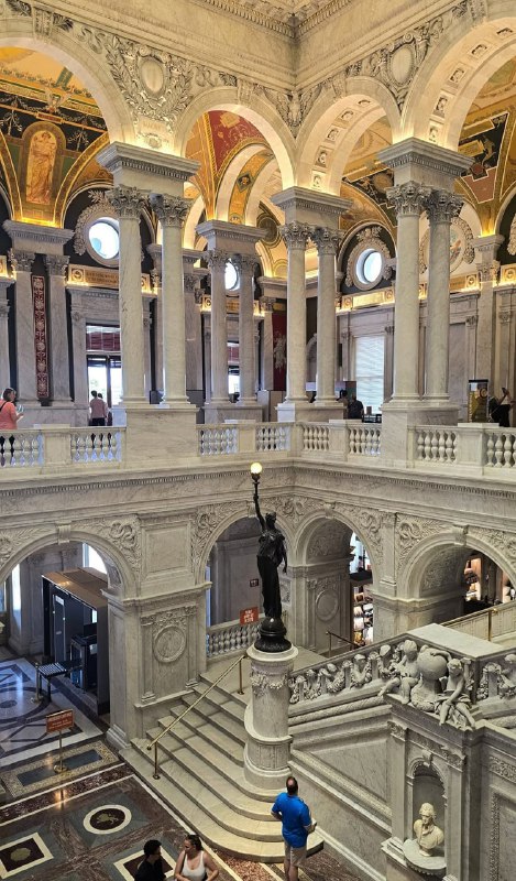 Лестничный пролёт и колоннада внутри здания Библиотеки Конгресса, снятые с угла — видна внутренняя лестница и посетители на уровнях.