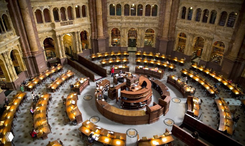 Круглый читальный зал Библиотеки Конгресса с рядами рабочих столов и лампами — панорамный вид на организованное пространство для чтения.