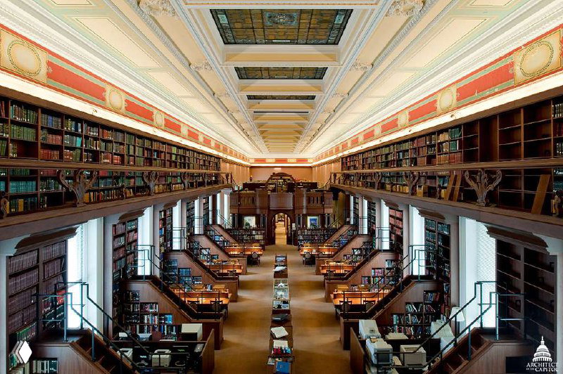 Длинный классический читальный зал с рядами столов, полками и высокими окнами — традиционная библиотечная архитектура и интерьер.