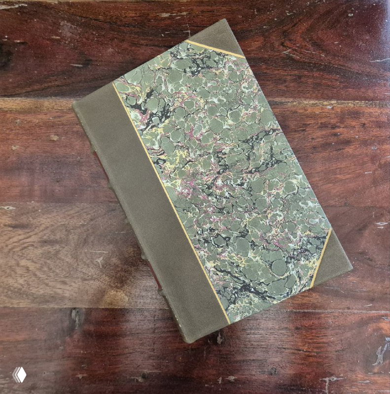 Вид сверху на мраморный переплёт книги: половинчатый кожаный корешок и мраморная обложка, книга лежит на деревянной поверхности.