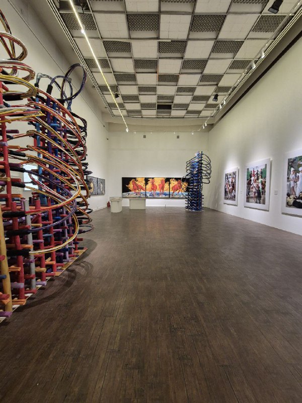 Широкий кадр большого выставочного зала ММОМА с инсталляциями, скульптурными колоннами и рядами фотографий на стенах.