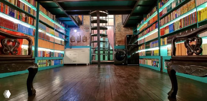 Широкий вид на зал с низкими полками, уставленными книгами по обеим сторонам, деревянный пол и уютная книжная атмосфера.
