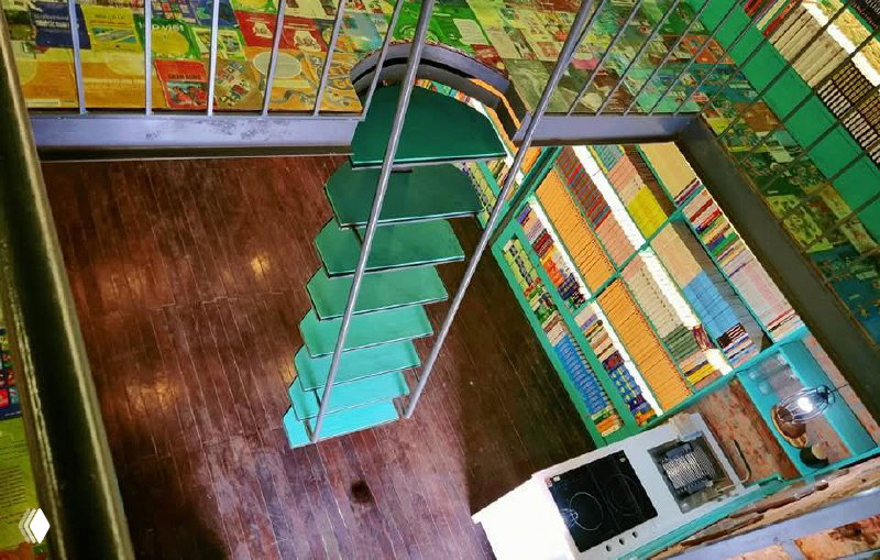 Вид сверху на лестницу-полку и рядами выстроенные книги, деревянный пол и организационная структура книжного пространства внутри дома.