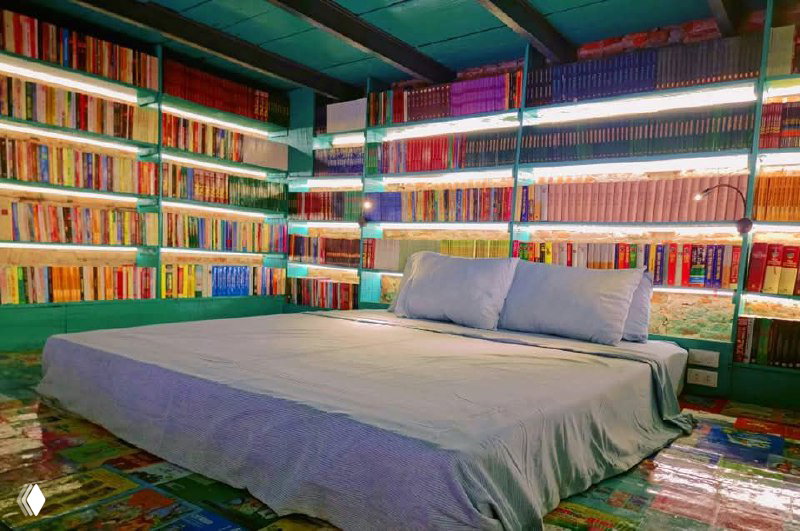 Спальная зона с низким матрасом и подушками, окружённая книжными полками со всех сторон, пространство для чтения и отдыха.