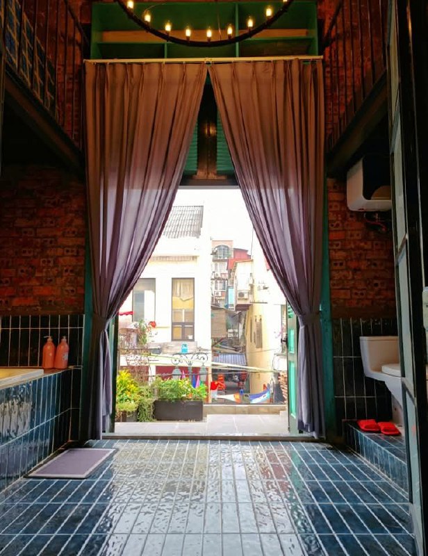 Открытая занавешенная арка, через которую видна городская улица; сочетание интерьера гостевого дома и уличной сцены старого квартала.