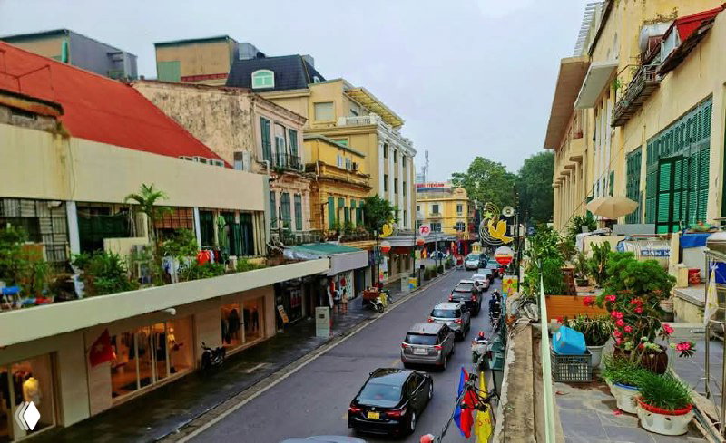 Панорамный вид на оживлённую улицу старого квартала Ханоя с магазинами, припаркованными автомобилями и балконами, вид с балкона дома.