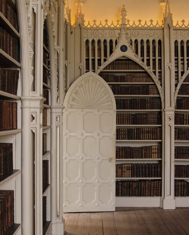 Белая резная дверь в нише между книжными полками библиотеки Strawberry Hill House: сочетание орнамента, деревянного пола и приглушённого света.