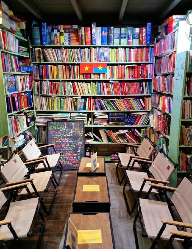 Уютная зона с креслами и столиками на деревянном полу перед стеллажами, пространство оформлено для чтения и небольших встреч.