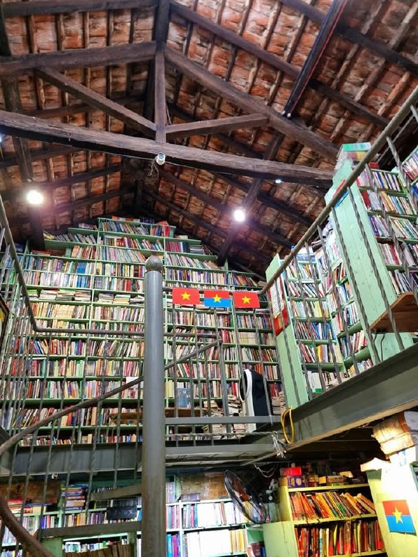 Высокий книжный зал с деревянной крышей и многорядными стеллажами, вид на второй уровень и полки, уходящие вверх под свод крыши.