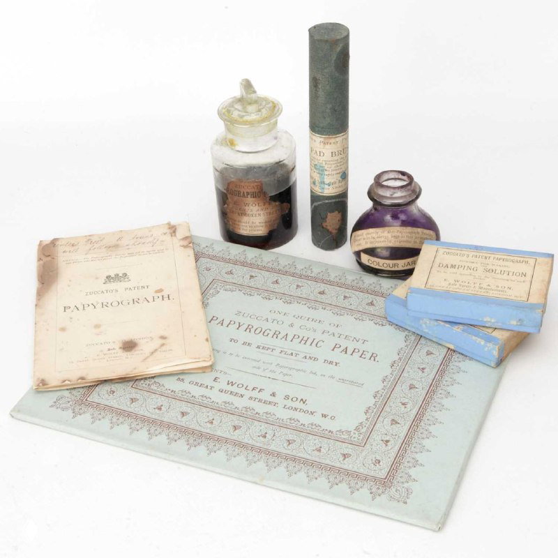 Набор расходных материалов: бутылочки с чернилами, ролик и пачка папирографической бумаги на столе рядом с метками и упаковкой.