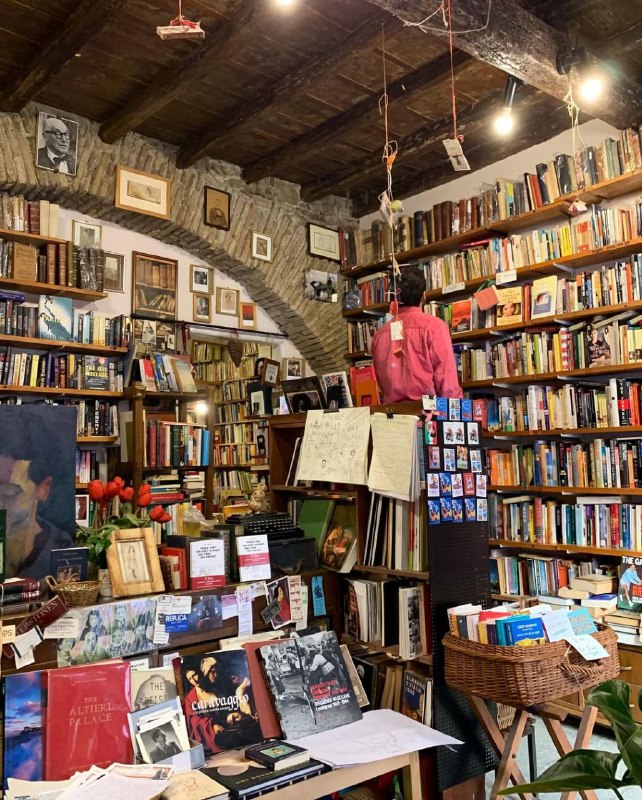 Интерьер Open Book: арочные каменные своды и низкий деревянный потолок, плотные ряды полок с книгами и посетитель, рассматривающий издания в полумраке.