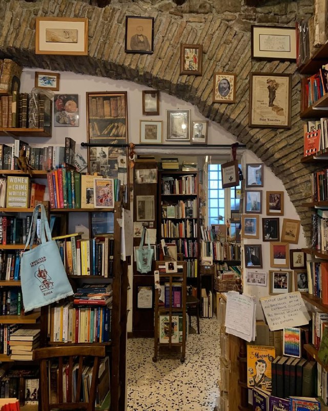 Узкий проход между стеллажами в Open Book: высокая плотность старых и новых изданий, плакаты и предметы декора создают уютную, слегка музейную обстановку.