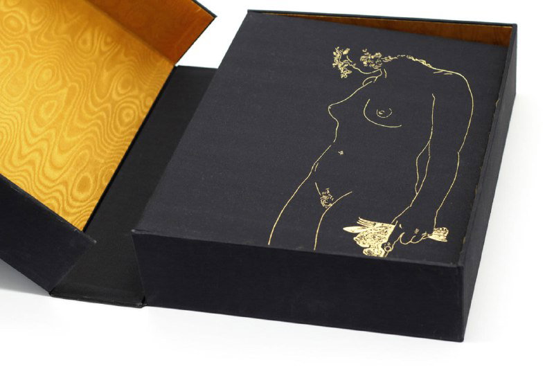 Открытая коробка с золотистым шелковым подкладом, внутри — обложка альбома с золотым контуром женской обнажённой фигуры в стиле Дали.