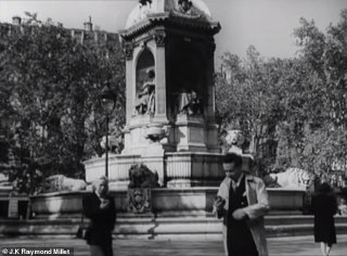 Чёрно‑белый кадр площади с монументом: прохожие с гаджетами в руках на фоне классической архитектуры, образ повседневности через призму будущего в кино.