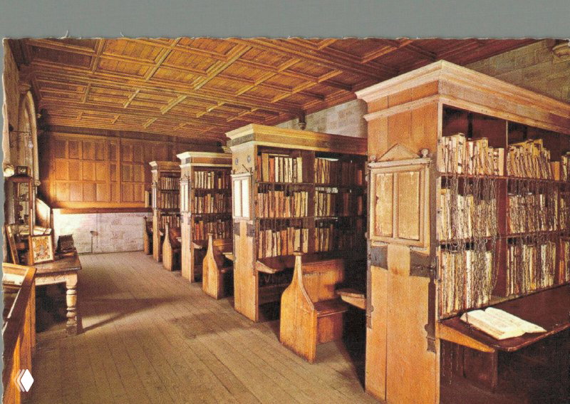 Интерьер старинной читальни при библиотеке: деревянные стеллажи и кафедры для чтения, полки с прикованными книгами и тёплая отделка.