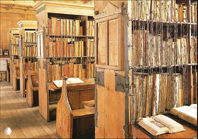 Ряд деревянных стеллажей с прикованными книгами в исторической библиотеке: видны переплёты, древесная отделка и проходы между полками.