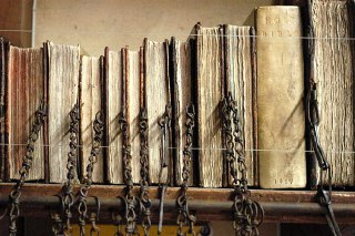 Крупный план корешков старых томов с прикреплёнными цепями: детали переплётов, ржавые звенья и текстуры бумаги видны вблизи.