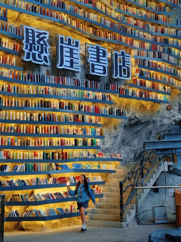 Фасад внутренней стены с полками и большим знаком на китайском; человек на лестнице даёт масштабу и ощущение высоты.