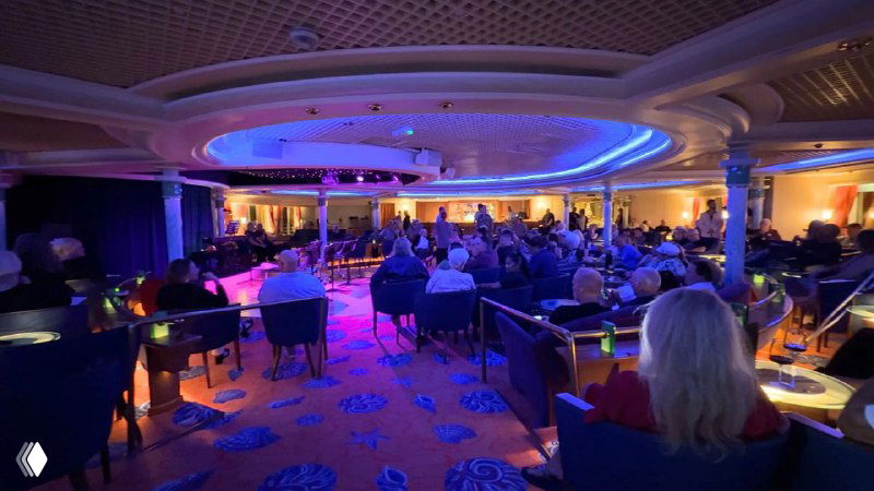 Вечерняя развлекательная программа в актовом зале лайнера: зрители в креслах, сценическое освещение и атмосфера шоу для пассажиров.