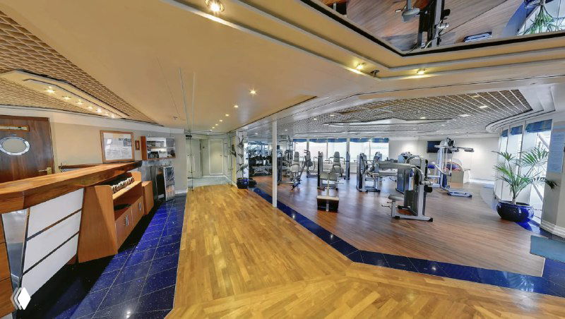 Фитнес-зал на корабле с тренажёрами, зоной для кардио и панорамными окнами — возможность поддерживать активность во время плавания.