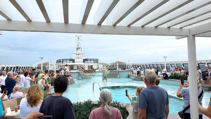 Палуба с бассейном, шезлонгами и группой людей у воды — центральная зона отдыха и купания на борту круизного судна Villa Vie.